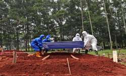 Workers in protective suits prepare to lower a coffin