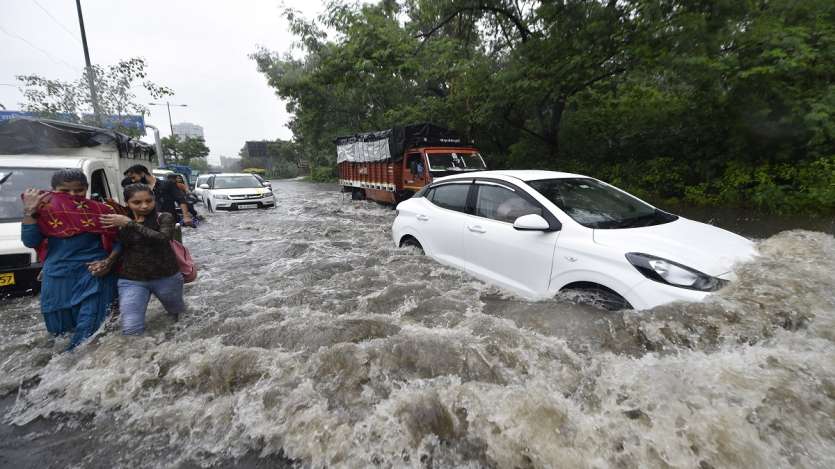 Commuters wade through a waterlogged street due to heavy rains, at Ring Road in New Delhi.